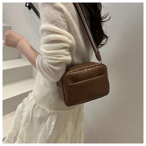 Detail view of deep brown woven texture crossbody bag with striped fabric strap on model