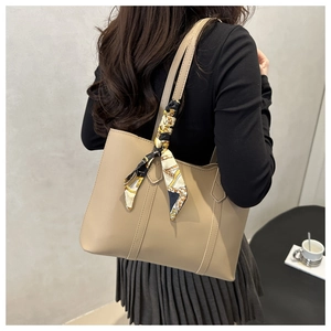 Detail of a large beige leather tote bag with a patterned silk scarf on the handle