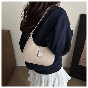 Detail of beige hobo bag with silver buckle worn over a casual blue sweatshirt