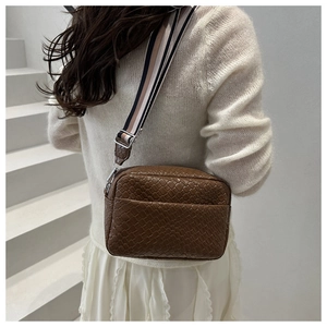 Detail of a dark brown woven leather crossbody bag with a striped wide fabric strap