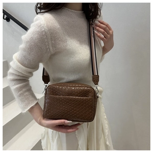 Brown woven crossbody bag with colorful striped strap shown on model in stair setting