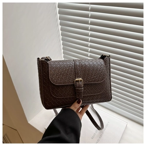 Detail of dark brown woven shoulder bag with gold metal buckle on a minimalist background
