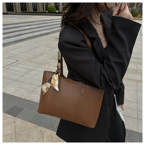Close-up of brown faux leather tote bag with printed silk scarf detail on handle