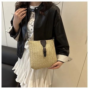 Detail of a straw crossbody bag featuring black leather straps and metal buckle closure