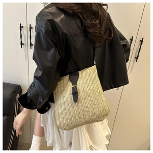 Detail view of woven straw shoulder bag with contrast leather strap and metal buckle