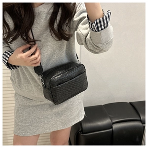 Detail of black woven texture crossbody bag with silver hardware and adjustable strap