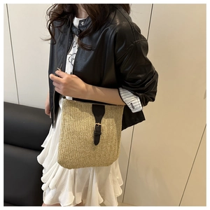 Detail of hand-woven beige straw tote bag with black leather strap and metal buckle