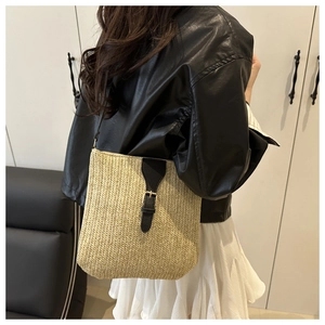 Detail of woven straw crossbody bag with black leather strap on a model outfit