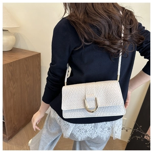 Detail of cream woven square bag featuring a gold U-shaped buckle on an adjustable strap