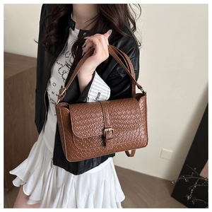 Close-up of brown woven leather handbag with golden buckle worn with a black jacket