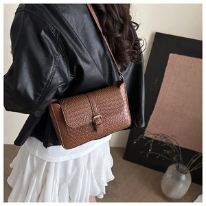 Brown woven texture crossbody bag with gold buckle shown on model in a modern room