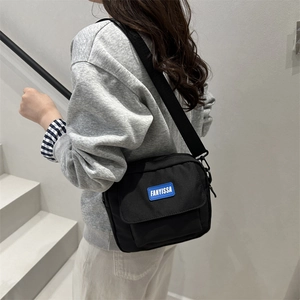 Minimalist black nylon crossbody bag with blue logo patch and wide adjustable shoulder strap