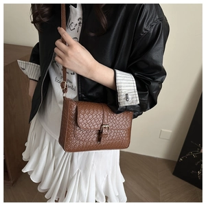 Close-up of brown woven texture crossbody bag with metal buckle on a stylish model