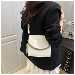 Detail of white leather shoulder bag with golden chains worn with a black suit