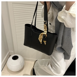 Detail of minimalist black tote bag with silk scarf on handle during daily commute