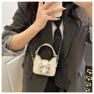 Mini bow handbag in cream PU leather with metal chain strap worn as a crossbody bag