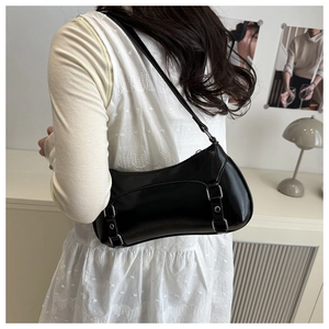 Detail of minimalist black faux leather shoulder bag with silver buckles and studs