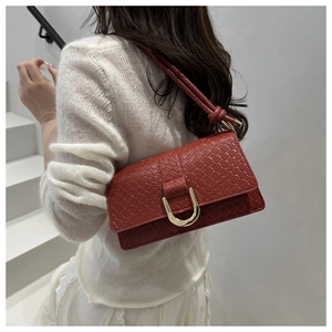 Detail of brick red woven texture shoulder bag with golden horseshoe buckle on model