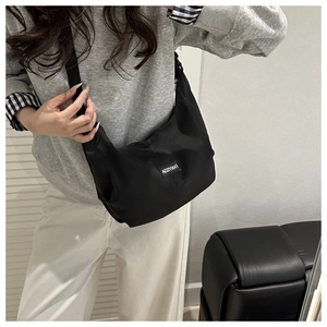 Detail of a black half-moon nylon crossbody bag with an adjustable strap on a model