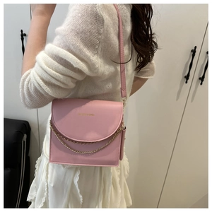 Close-up of pink crossbody bag with double gold chains on model against white background