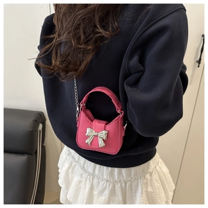 Close-up of bright pink mini bag with silver bow ornament and chain strap on model