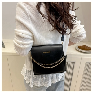 Detail of matte black crossbody bag featuring dual gold chain and leather shoulder strap