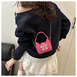 Close-up of a mini pink handbag with silver bow detail and metal chain on a model