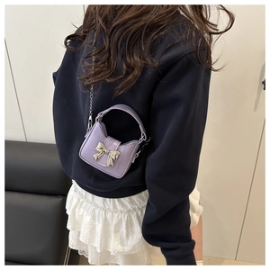 Model showing a mini light purple crossbody bag with silver bow and chain strap