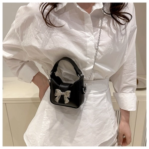 Detail of a mini black leather crossbody bag with a large silver metal bow accessory
