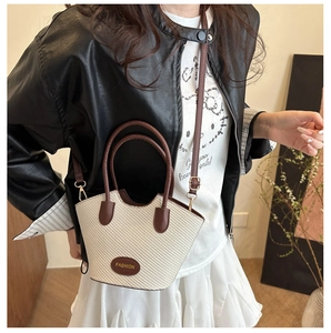 Détail d'un sac seau tissé avec poignées en cuir marron et bandoulière réglable
