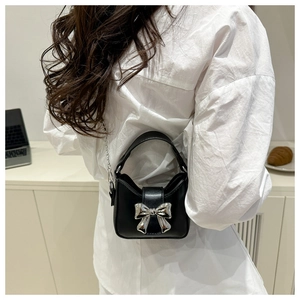Detail of a chic black mini bag with a silver metallic bow and elegant chain strap