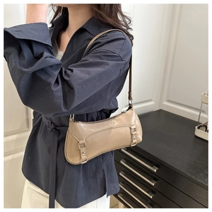 Detail of a chic beige baguette bag with shiny finish and silver buckle on model