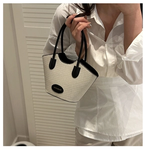 Detail of hand-woven straw tote bag with black leather handles and fashion logo