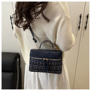Détail du sac boîte en tweed bleu marine avec garnitures dorées porté sur un pull en maille
