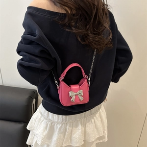 Mini pink bow handbag with metallic chain strap shown on a model in a minimalist setting