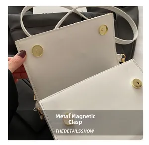 Detail of the high-quality gold magnetic buckle closure on a white woven crossbody bag