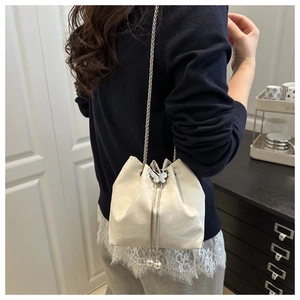 Close-up of white bucket bag featuring butterfly metal buckle and pearl tassel charms