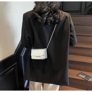 Detail of silver crocodile-embossed crossbody bag with metallic chain strap worn on shoulder