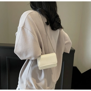 Detail of white crocodile embossed mini crossbody bag with sleek metal chain strap