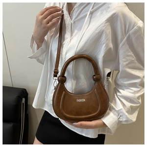 Detail of a brown crescent bag featuring metal strap rings and fashion text on PU leather