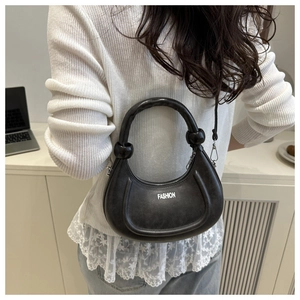 Close-up of black crescent bag with FASHION text shown on model in indoor setting