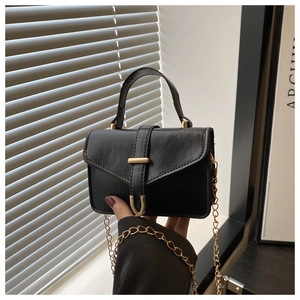 Detailed macro view of black faux leather mini bag with gold V-shaped buckle and chain strap