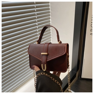 Detail of dark reddish brown faux leather mini bag with gold chain and U-shaped buckle