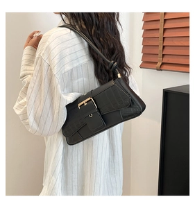 Detail of black faux crocodile skin shoulder bag with gold square buckle worn under arm