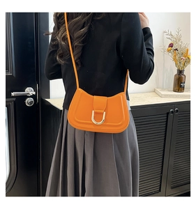 Detail of bright orange saddle bag with gold U-buckle worn as a shoulder bag