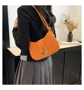 Detailed view of bright orange leather shoulder bag with gold horseshoe buckle on black blazer