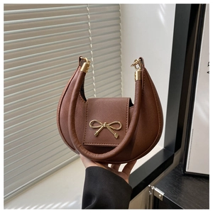Detail of a brown crescent baguette bag with a golden bow and fine leather texture