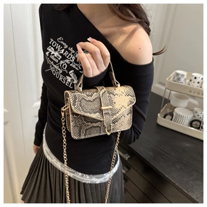 Detail shot of a snake pattern handbag with gold hardware and chain strap on a model