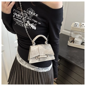 Detail of silver metallic crossbody bag with hard handle and chain strap worn by a model