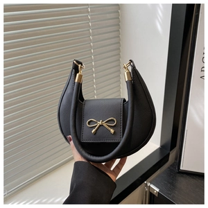 Detail of black dumpling bag with textured faux leather and gold bow embellishment